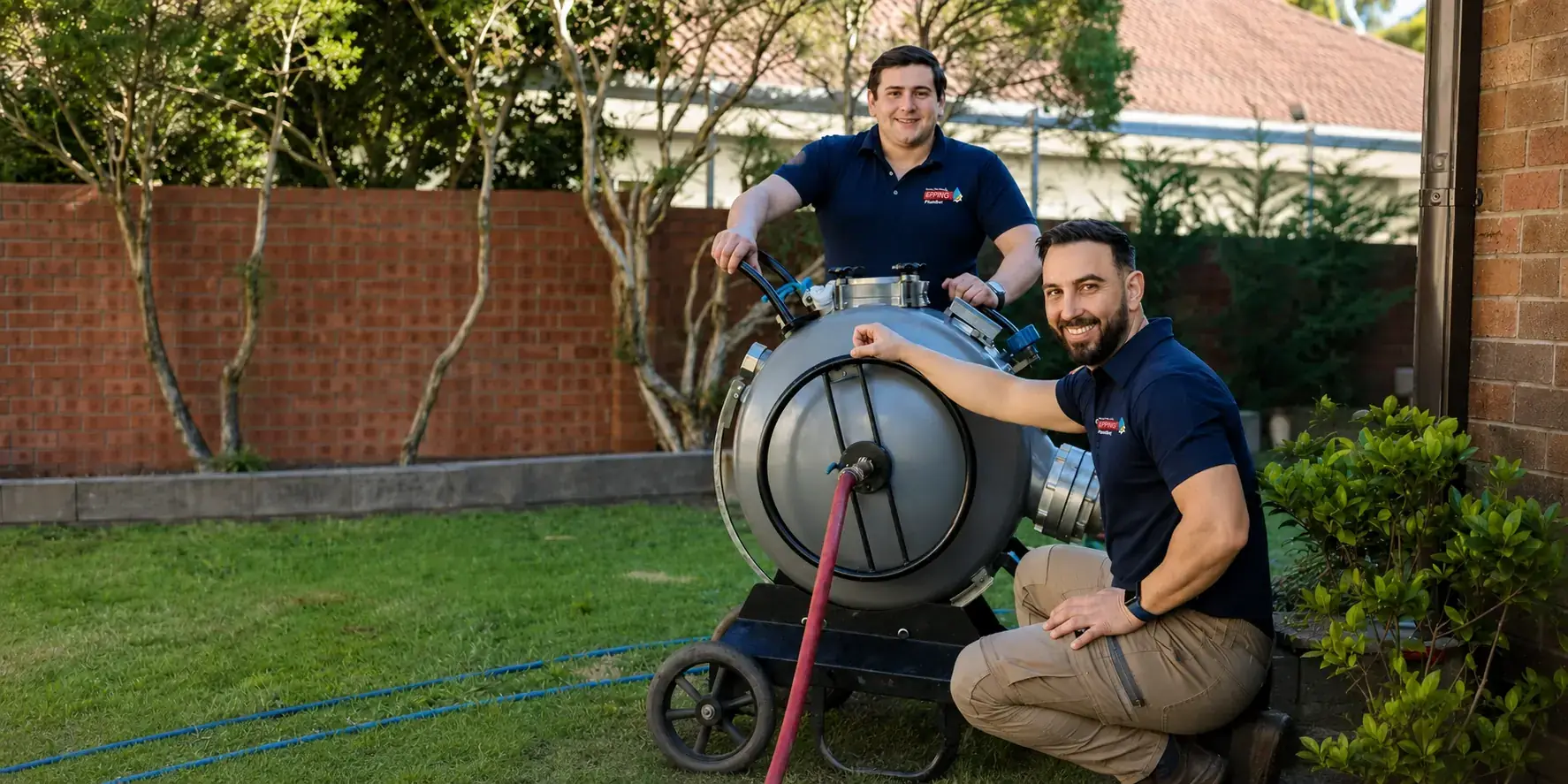 Two Epping plumbers with a drain cleaning machine in a backyard